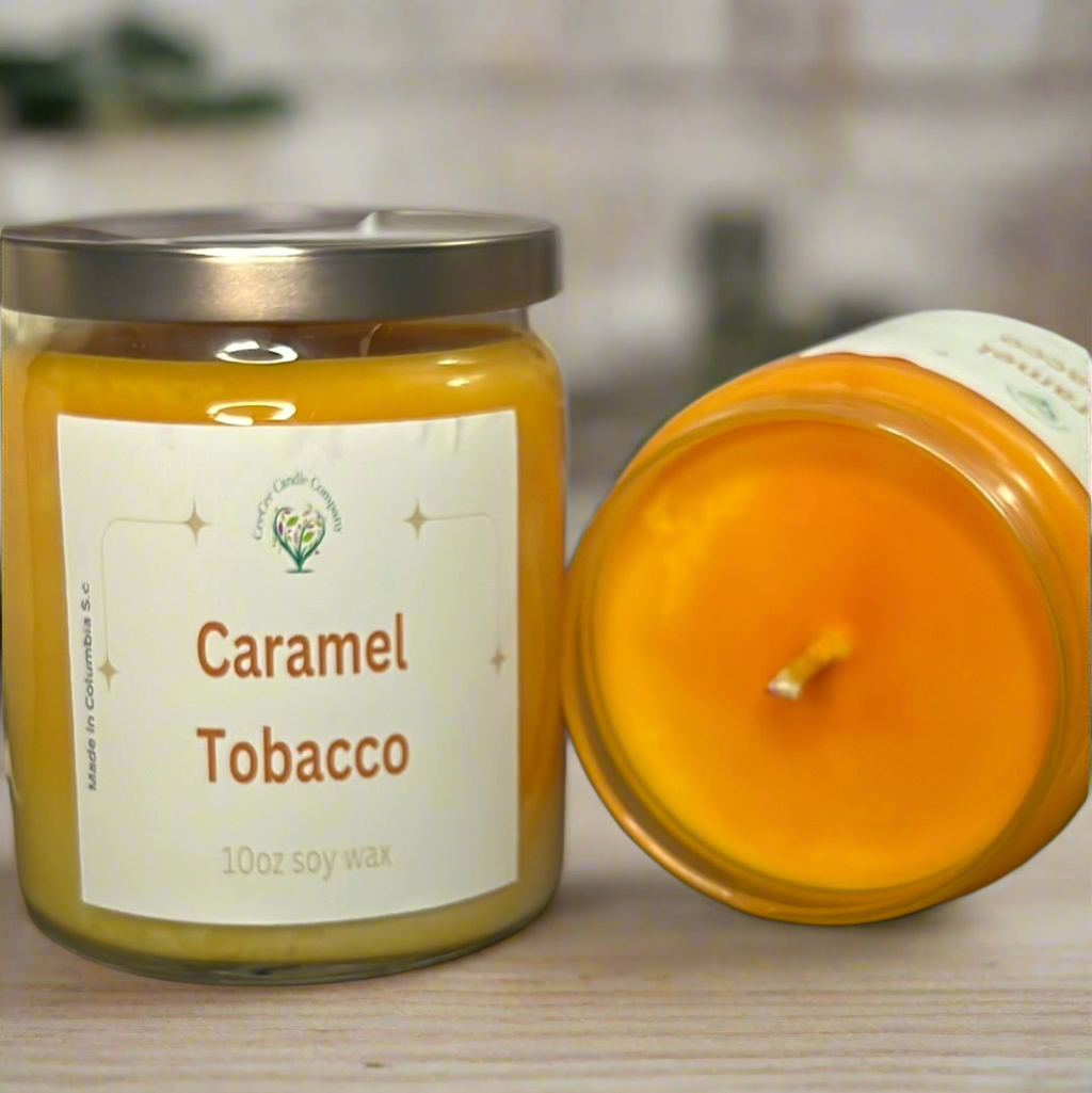 Two yellow candles from the CeeCee Candle Company Signature Apothecary Collection, labeled "Caramel Tobacco," feature white labels with green and gold accents. One stands upright with a silver lid; the other lies on its side, wick visible.