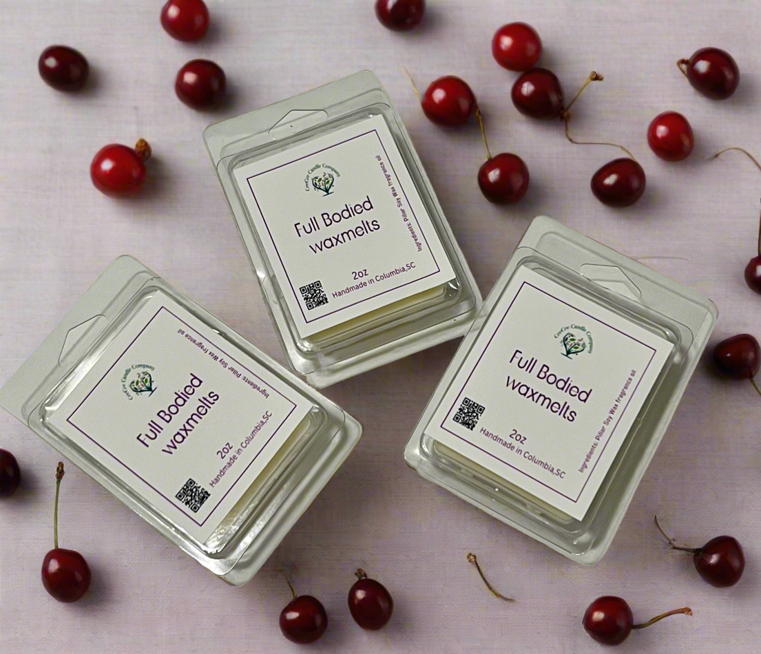 Three packs of CeeCee Candle Company Heart Shaped Wax Tarts, made with soy wax, sit on a light surface surrounded by cherries. The clear packaging shows white labels, heart-shaped melts, and a small QR code on each pack.