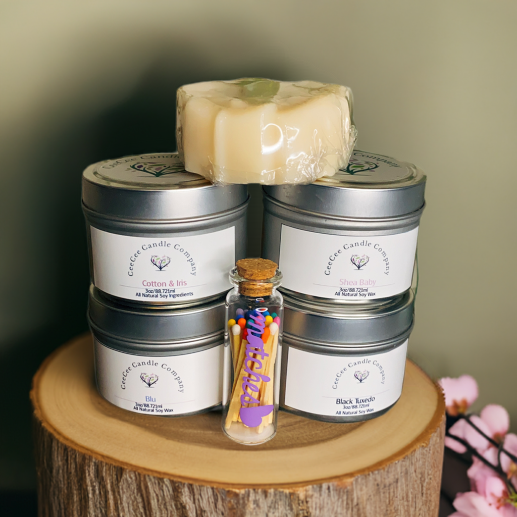 The CeeCee Candle Company Gift Box by CeeCee Candle Company includes four soy candle tins, a wrapped soap bar, and a jar of colorful matches on wood, accented with pink flowers—an eco-friendly self-care gift.