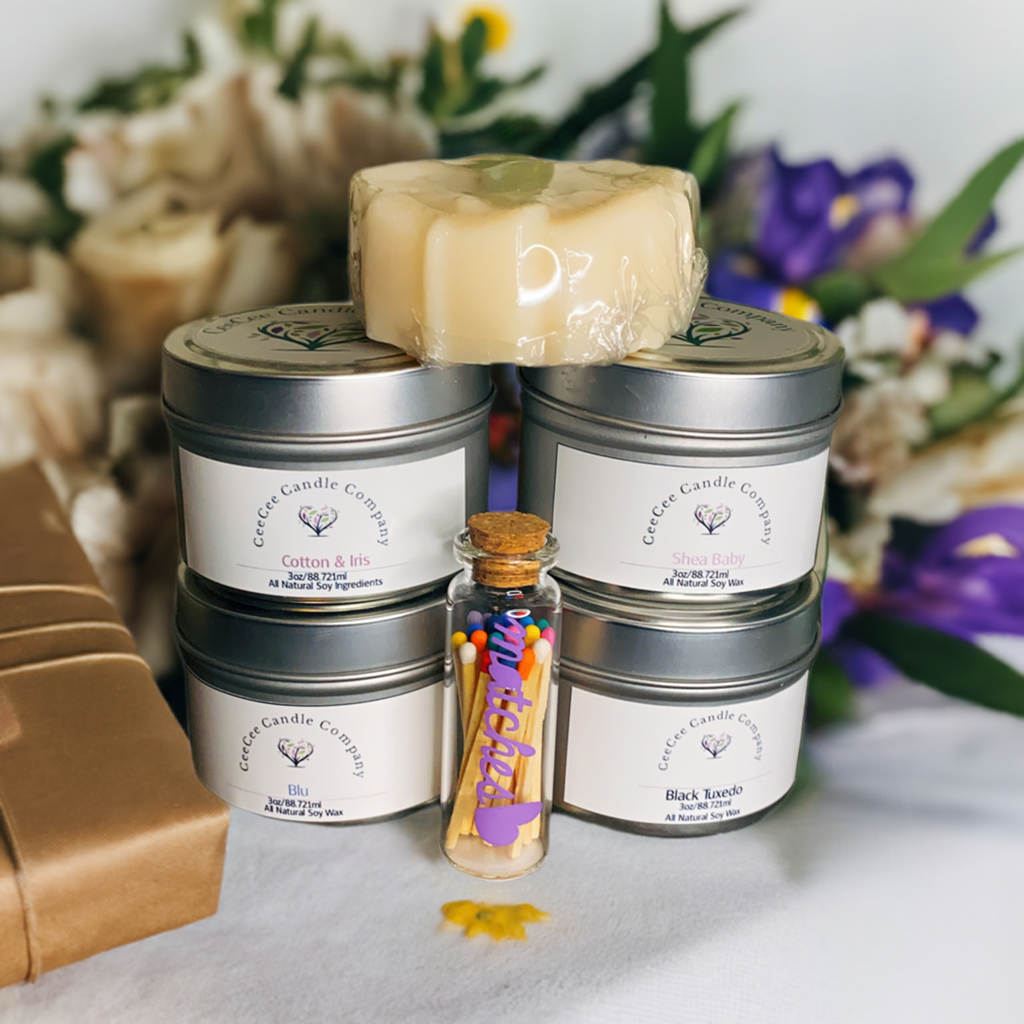 The CeeCee Candle Company Gift Box by CeeCee Candle Company features four labeled soy candles in eco-friendly packaging stacked in a pyramid, a wax melt on top, and a glass jar of matches in front, with flowers and a self-care gift behind.