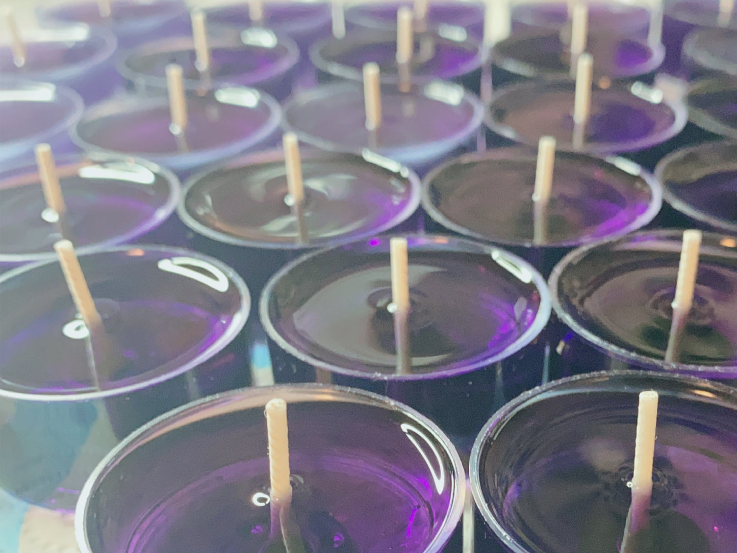 CeeCee Candle Company’s Soy Wax Tea Light Candles are eco-friendly and purple, featuring wooden wicks. Arranged in neat rows, their glossy surfaces reflect light, showcasing vibrant color and aromatherapy benefits.