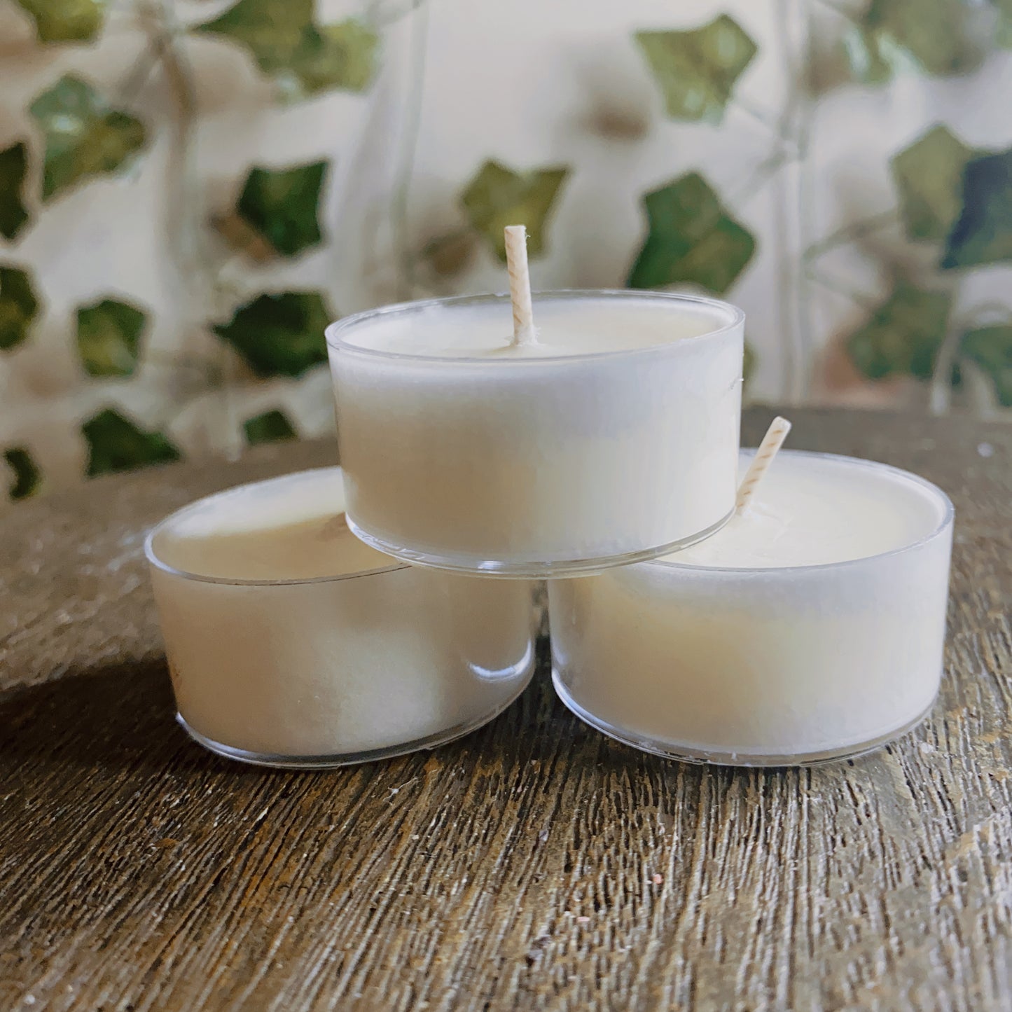 Three CeeCee Candle Company Soy Wax Tea Light Candles in clear holders are arranged on wood, framed by green ivy leaves, offering subtle aromatherapy and an eco-friendly ambiance.