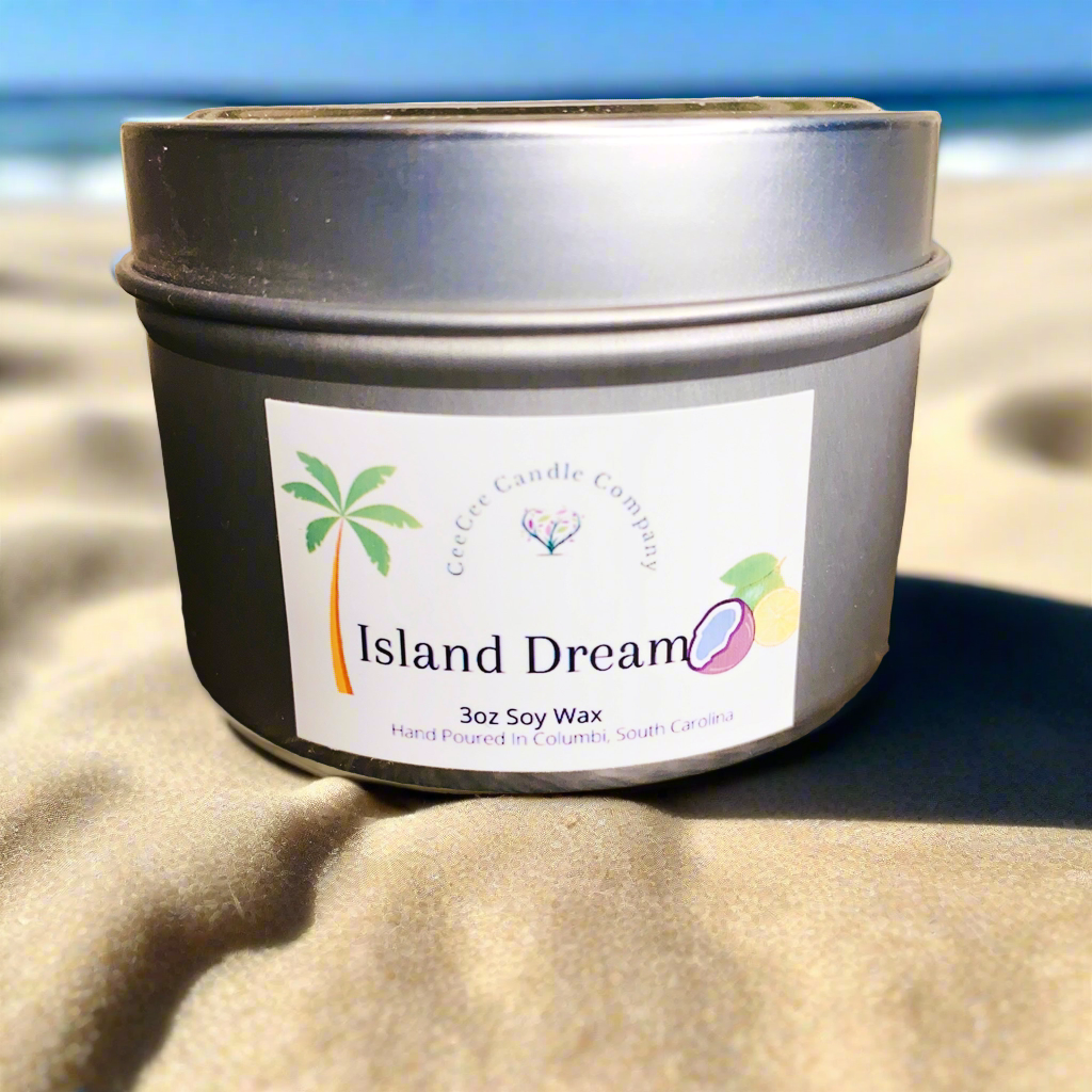 The CeeCee Candle Company Travel Size Soy Candle, labeled "Island Dream" with palm tree and coconut art, sits on sandy beach with ocean in the background—a perfect mood-boosting fragrance for your next getaway.