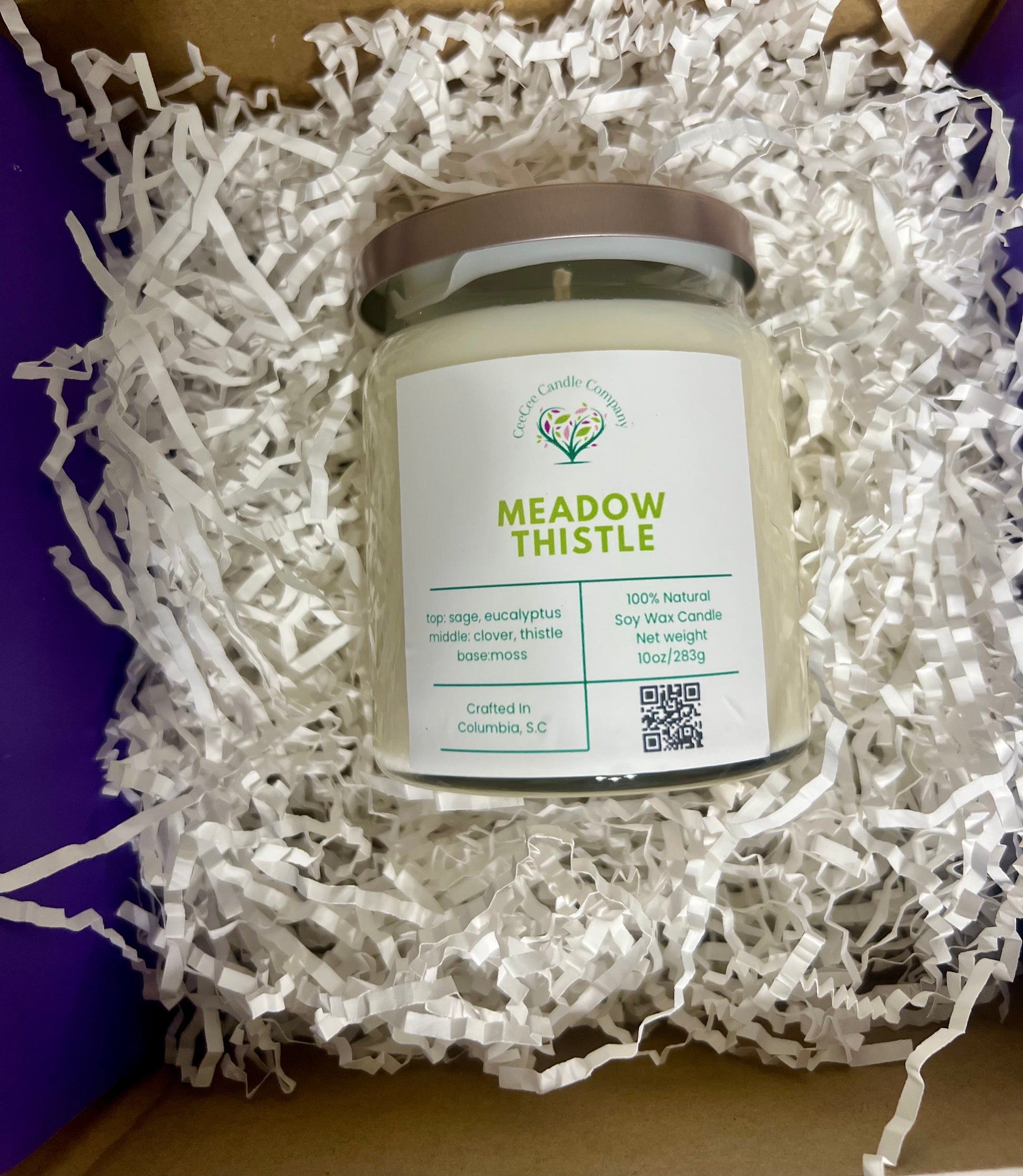 A CeeCee Candle Company Signature Apothecary Collection jar candle, nestled in white crinkle paper, is made with natural soy wax and premium oils. Its label highlights sage, eucalyptus, clover, thistle, and moss for a soothing scent.