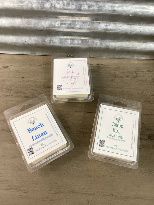 The Build Your Own Wax Melts Bundle from CeeCee Candle Company features Beach Linen, Pink Sugar Crystals, and Citrus Kiss packs displayed on wood with a metal backdrop—customize your perfect scent set for any space.