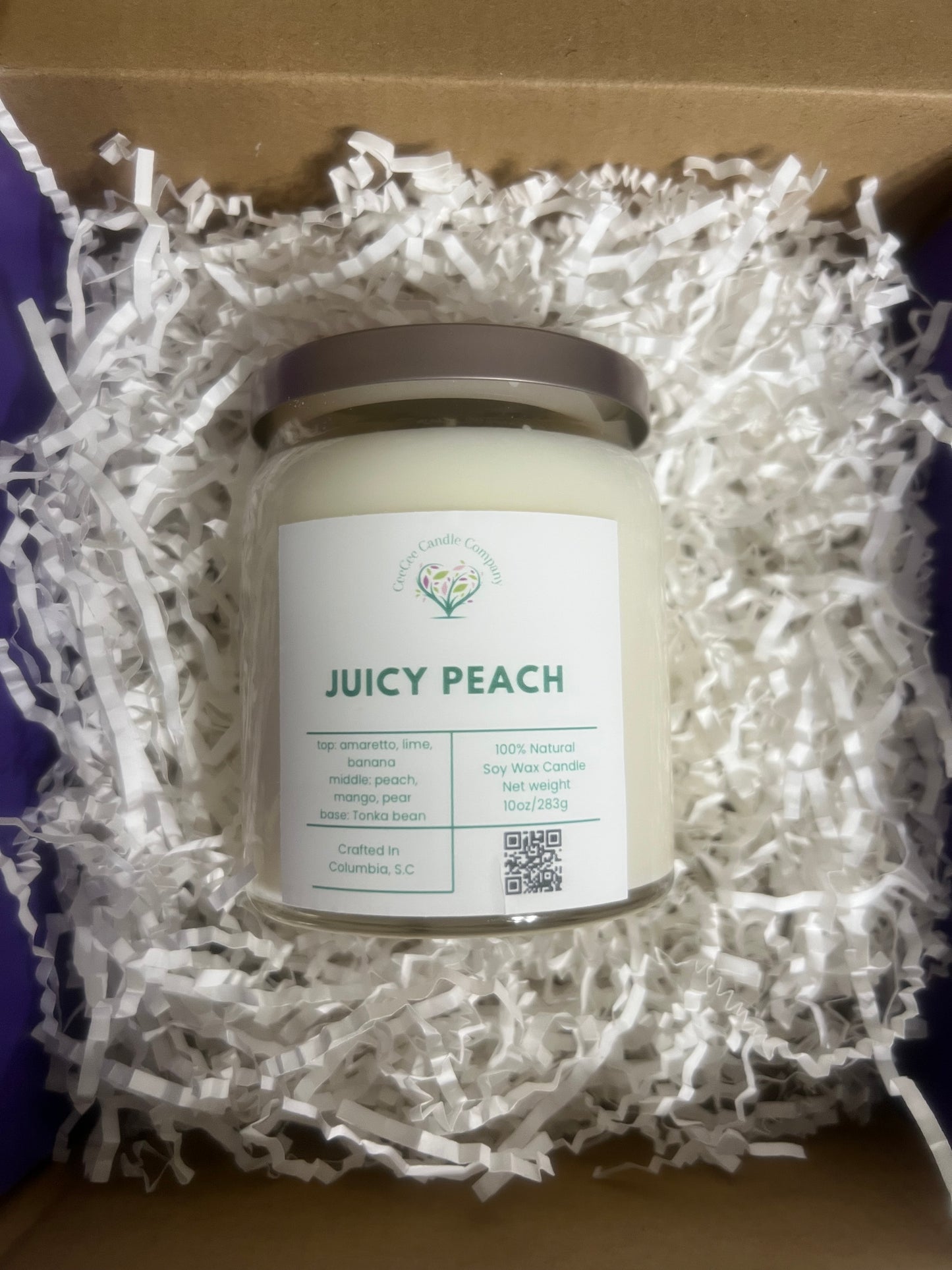 The CeeCee Candle Company Signature Apothecary Collection jar candle sits in white crinkle paper. Handcrafted in Columbia, SC, this soy candle features premium oils with notes of amaretto, peach, mango, and tonka bean.