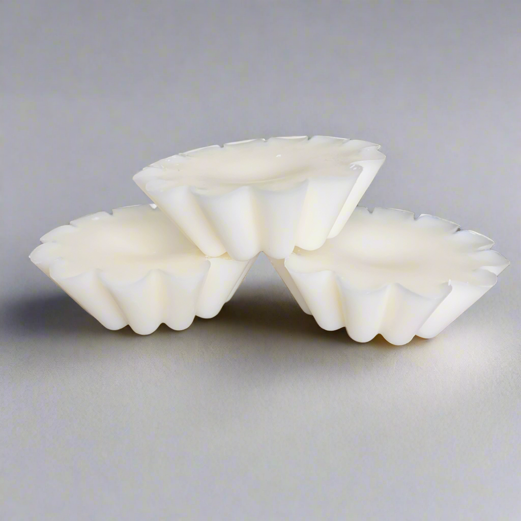 Three white, fluted Candle Tart Melts from CeeCee Candle Company are stacked in a small pyramid on a plain, light gray surface under soft lighting with no visible background details.