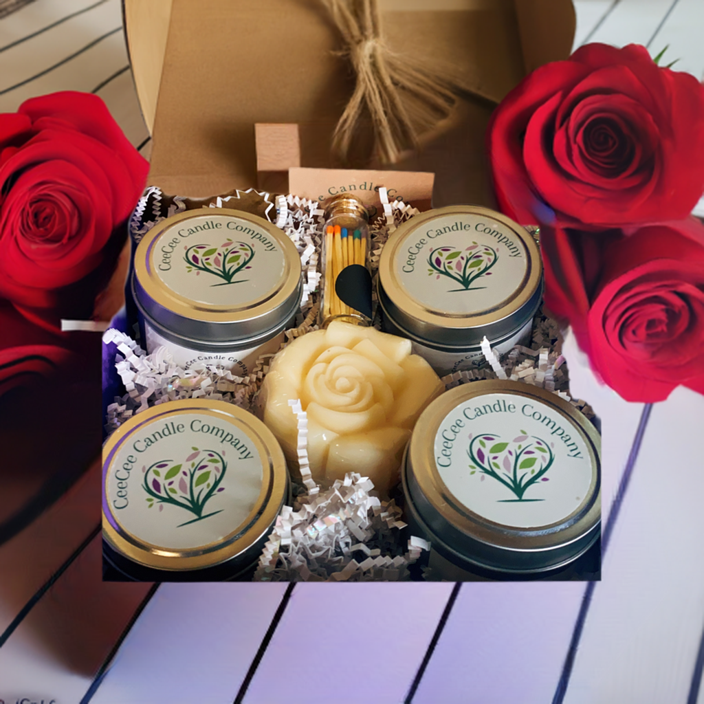 The CeeCee Candle Company Gift Box features four soy candles, a rose-shaped candle, matches, and white crinkle paper in eco-friendly packaging by CeeCee Candle Company. Three red roses surround the box on a striped surface.