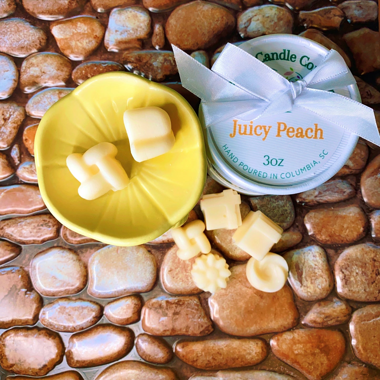 The Wax Melts Gift Box by CeeCee Candle Company features cream-colored, Pillar Blend Soy Wax melts in various shapes, displayed in a yellow dish and a "Juicy Peach" tin on a textured, stone-patterned surface.