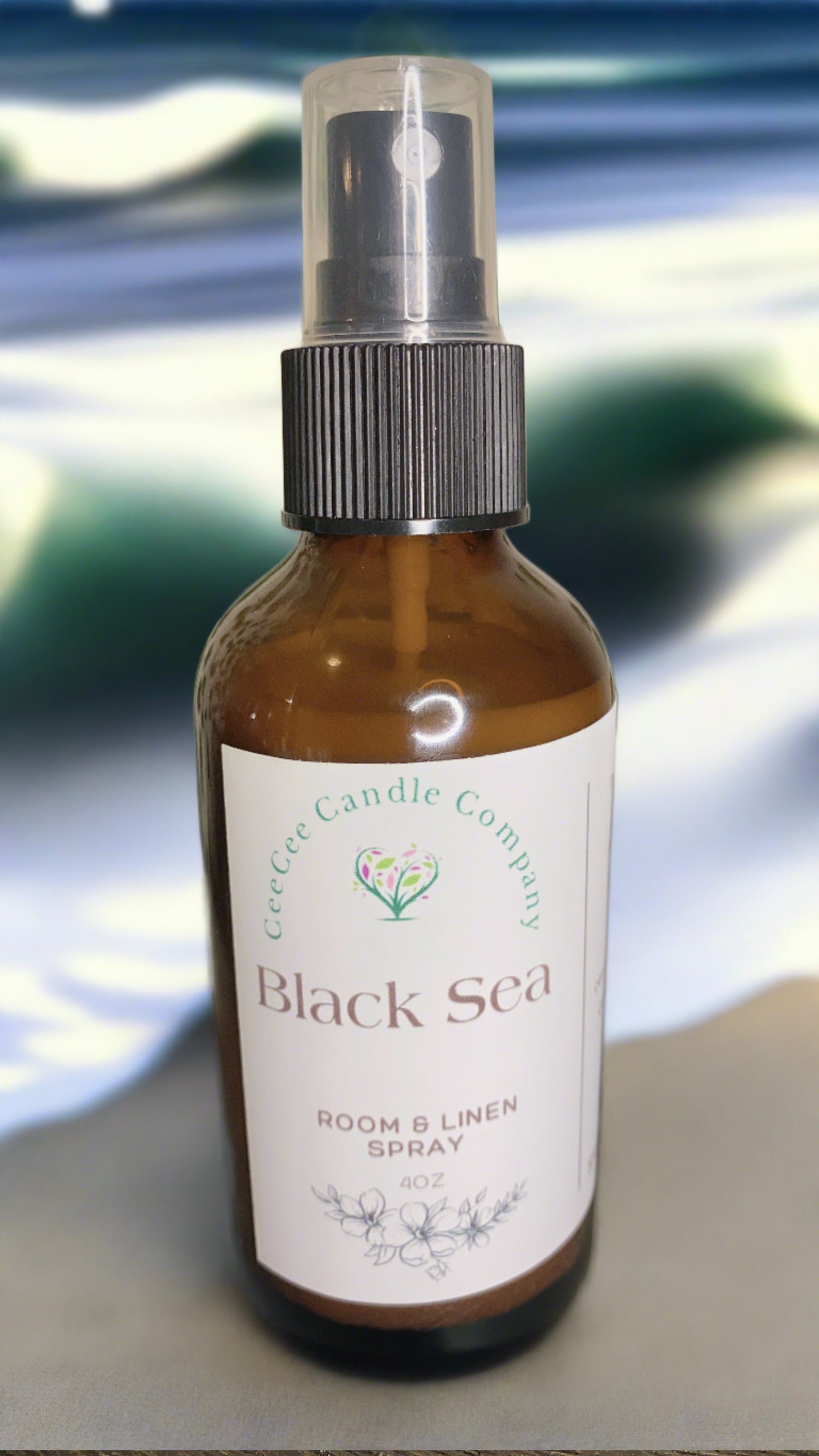 A brown spray bottle labeled "CeeCee Candle Company Room & Linen Spray – Clean, Long-Lasting Scents" stands before a blurred blue and white background, highlighting one of CeeCee Candle Company's signature all-natural fragrances.