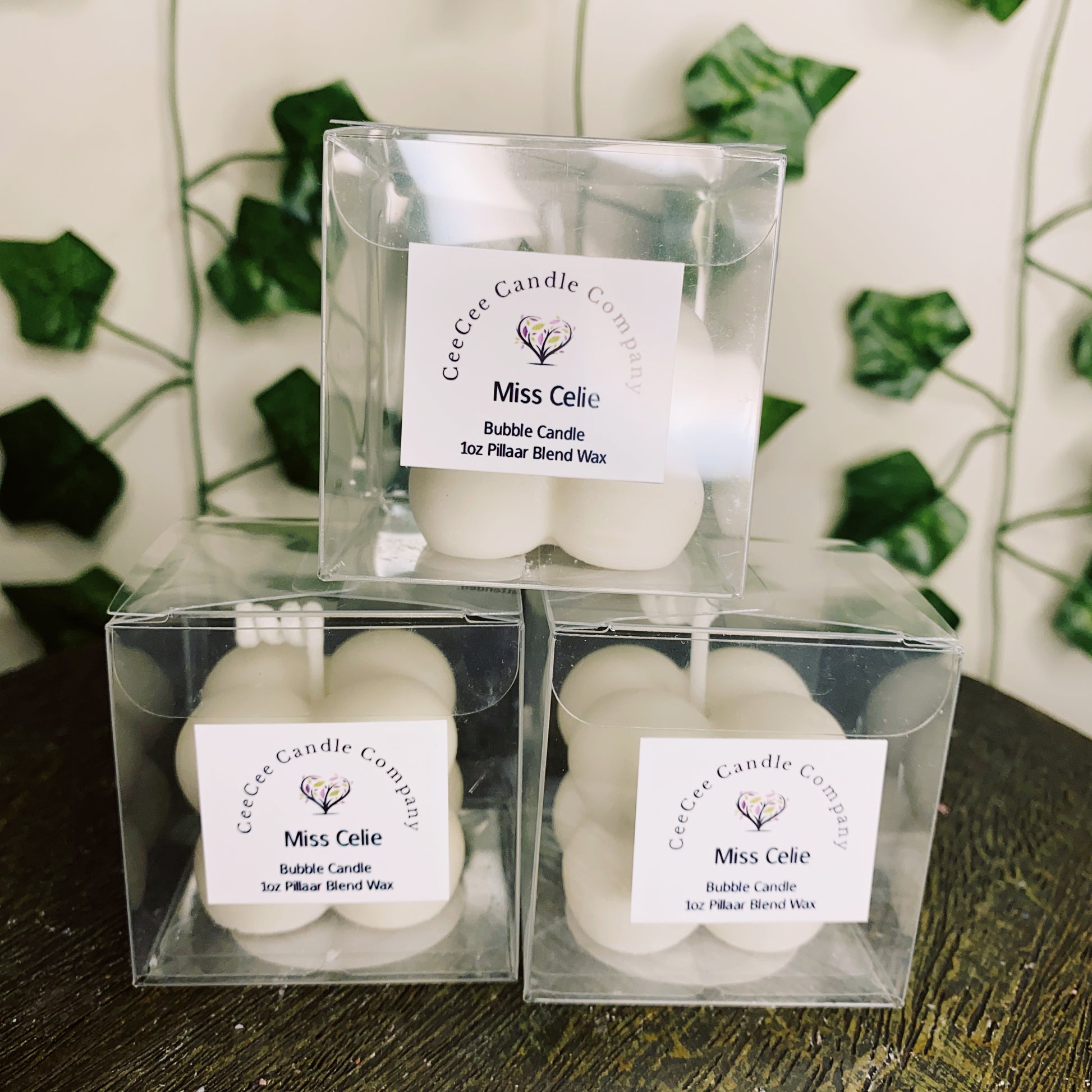 Three white Bubble Candles with glass dishes by CeeCee Candle Company sit in a pyramid before green vines—perfect for burning with your favorite fragrance oils.