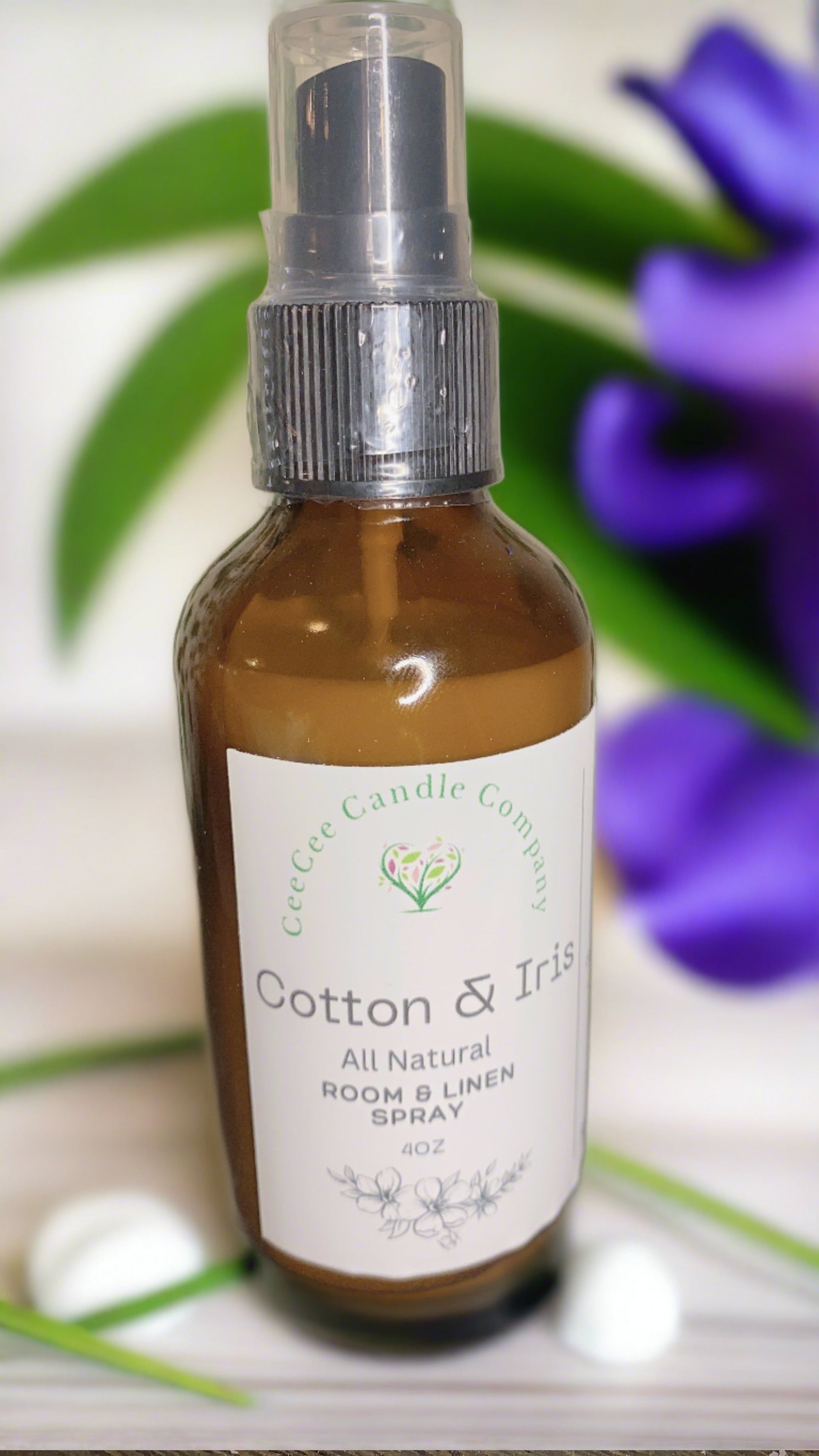 A brown bottle of CeeCee Candle Company Room & Linen Spray – Clean, Long-Lasting Scents stands before a blurred green and purple floral background, showcasing the signature fragrance by CeeCee Candle Company.