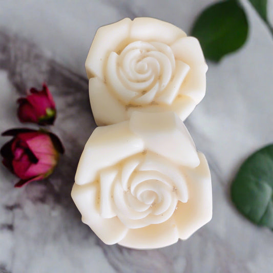 Two white Rose Candle Tart Melts from CeeCee Candle Company are displayed on marble, accompanied by red rosebuds and a green leaf, highlighting their delicate wax blend.