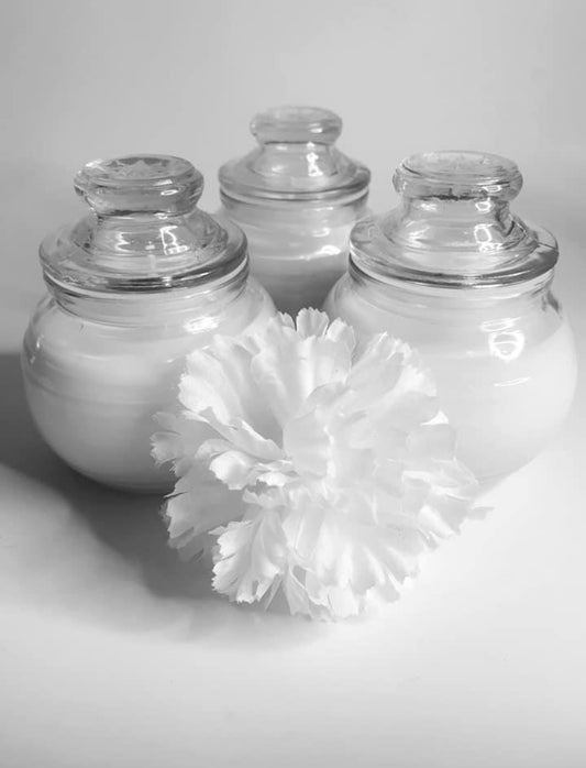 Three Spa Soy Candles by CeeCee Candle Company, in glass jars with lids, are grouped together. In front is a large white carnation. The black-and-white image highlights the elegant arrangement.