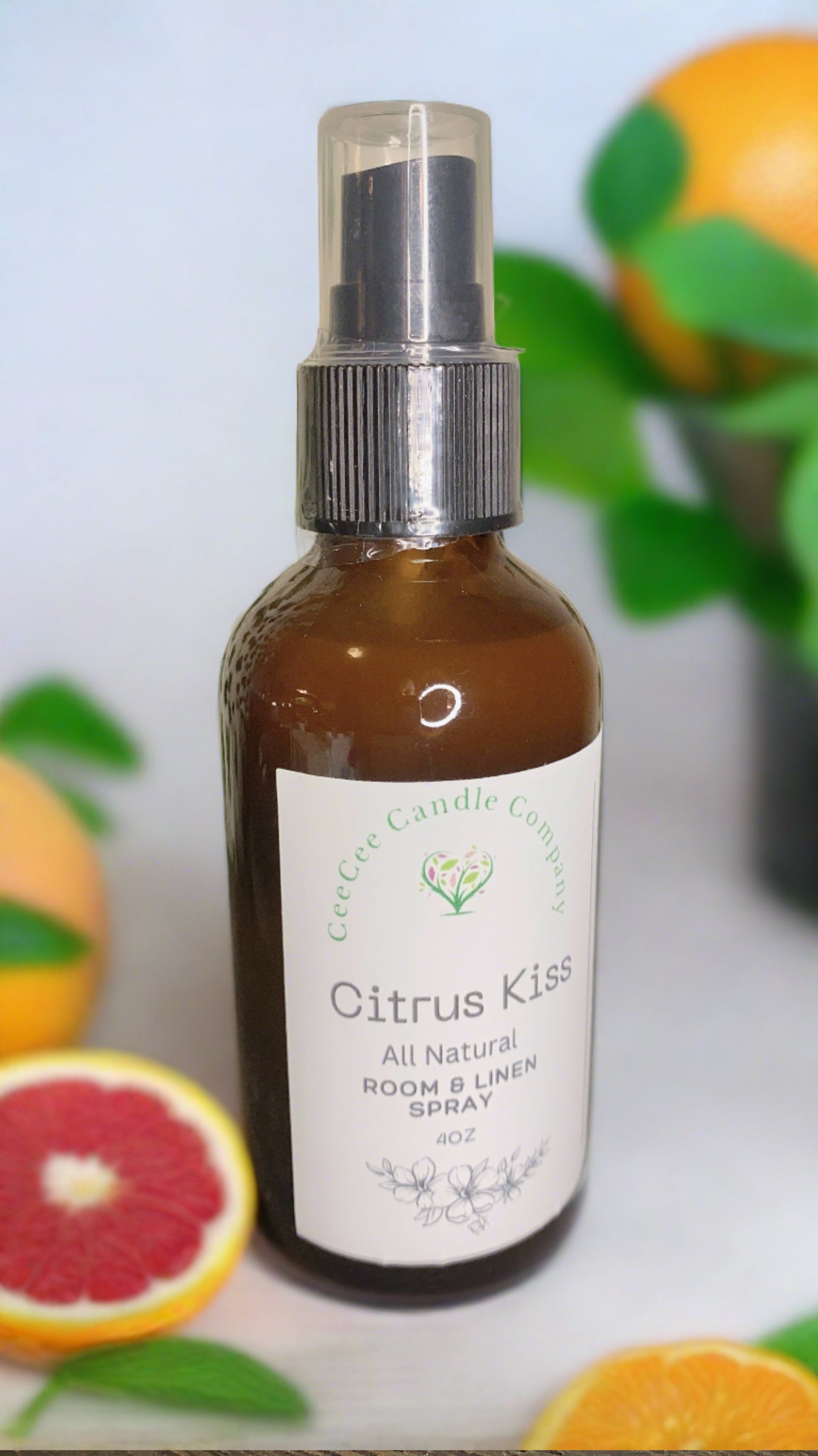 A brown spray bottle labeled "CeeCee Candle Company Room & Linen Spray – Clean, Long-Lasting Scents" sits among fresh oranges and sliced grapefruit with green leaves, capturing the refreshing essence of CeeCee Candle Company.